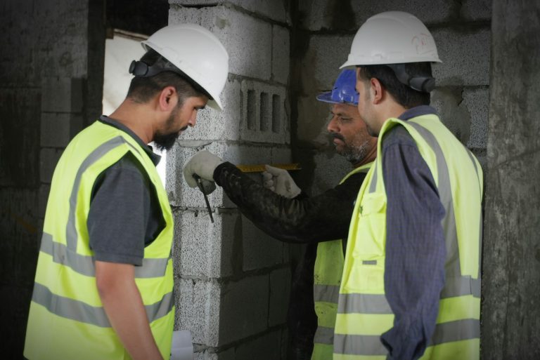 Three workers measuring a block wall