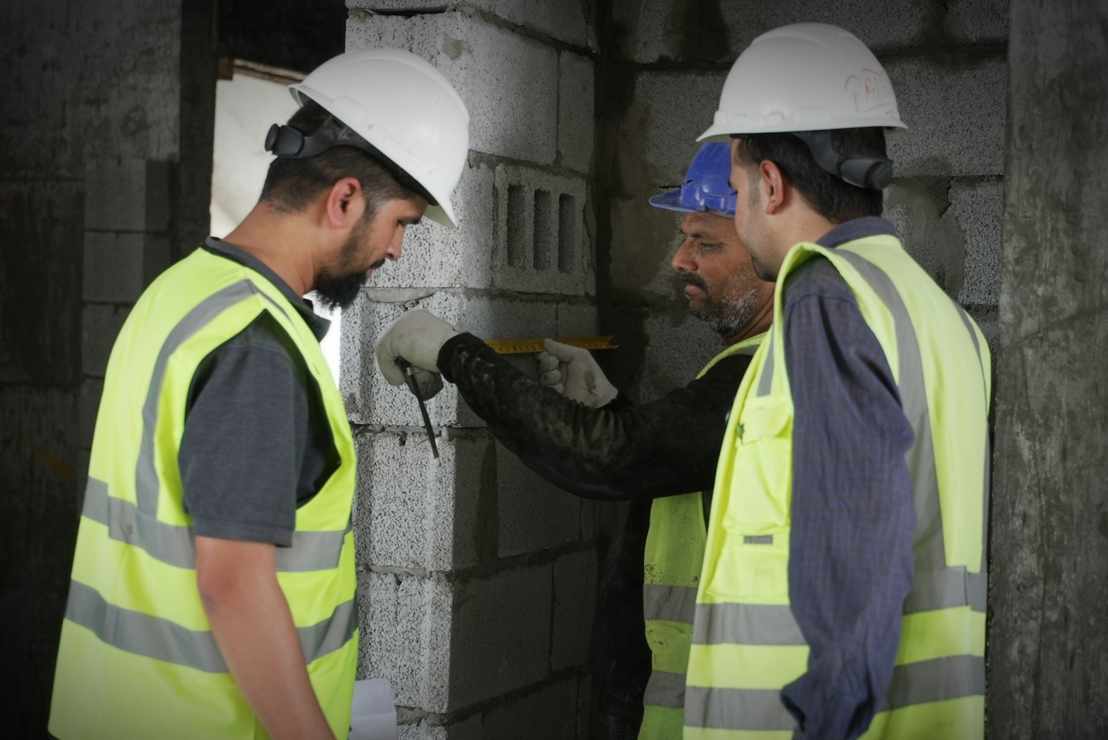 Three workers measuring a block wall