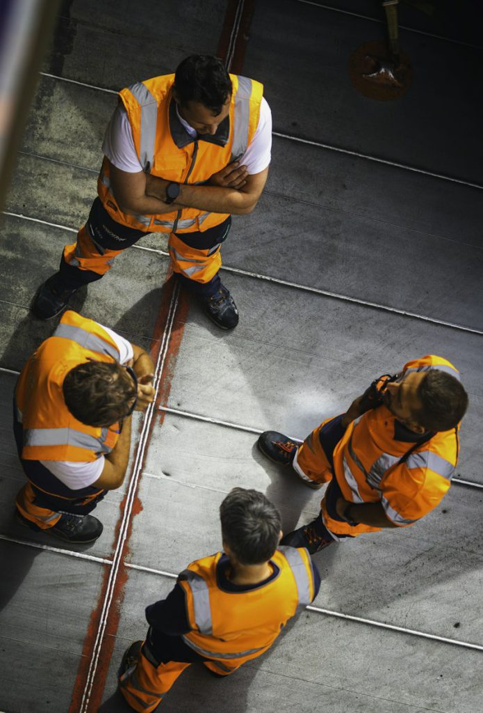 Workers in orange high-visibility vests on an industrial floor